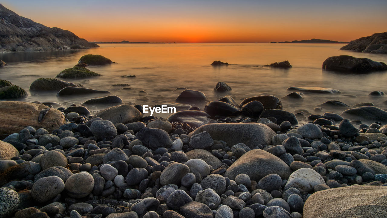 Rocks on beach against sky during sunset