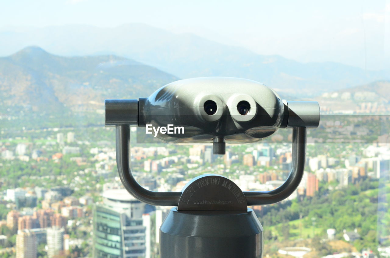 CLOSE-UP OF COIN-OPERATED BINOCULARS AGAINST CITYSCAPE IN MOUNTAINS