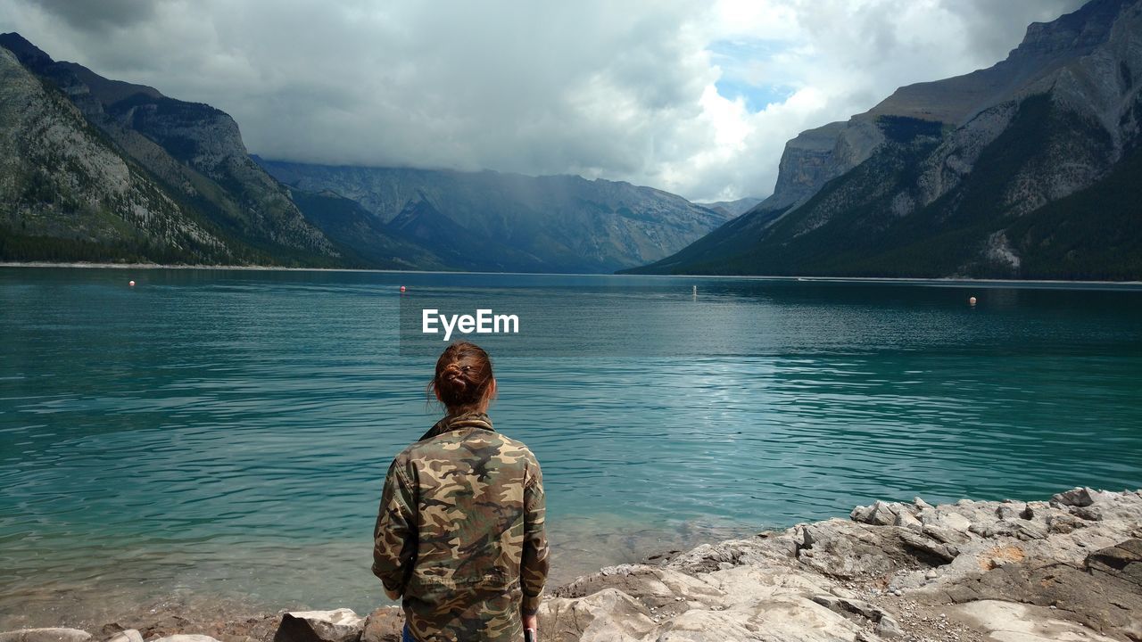 Rear view of woman standing at lakeshore against mountains