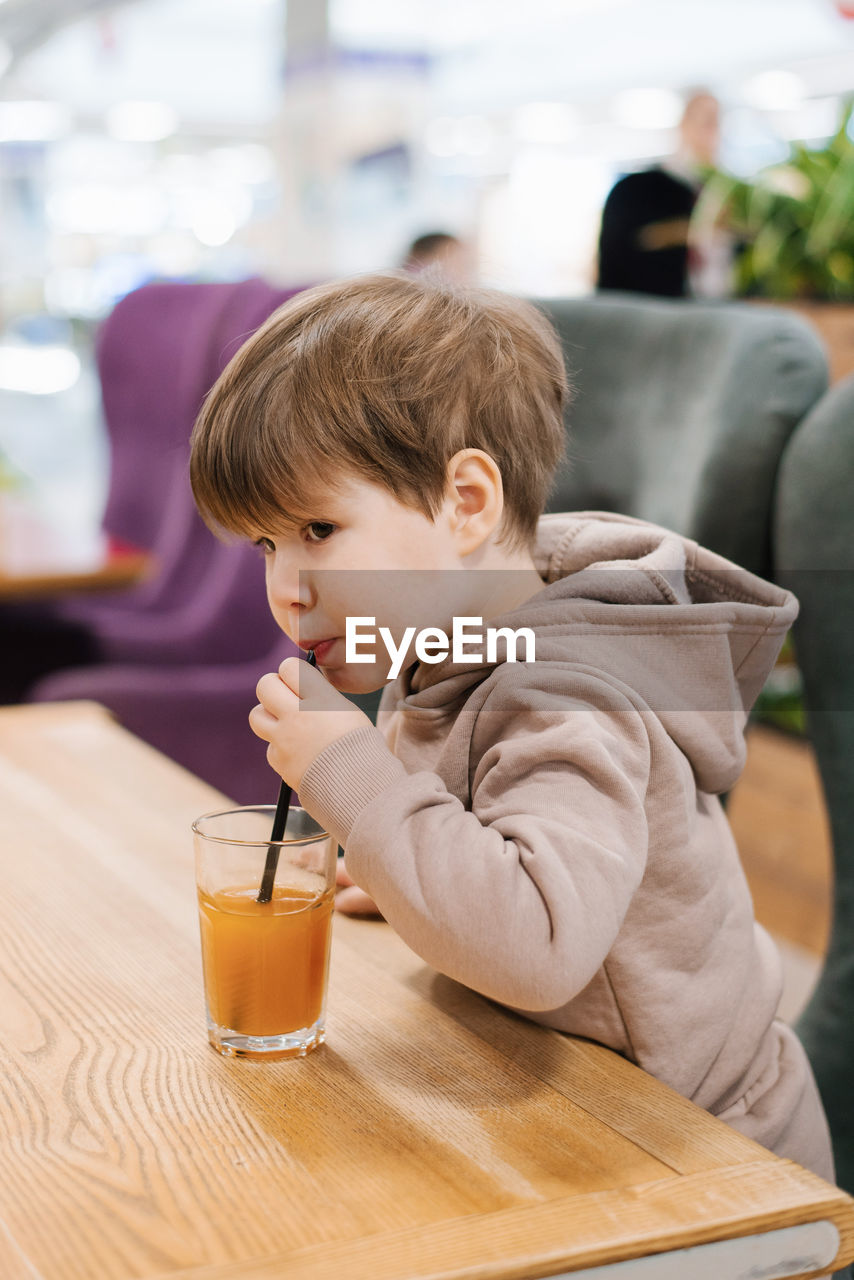 Little boy child drinks juice from a straw while sitting at a table in a cafe