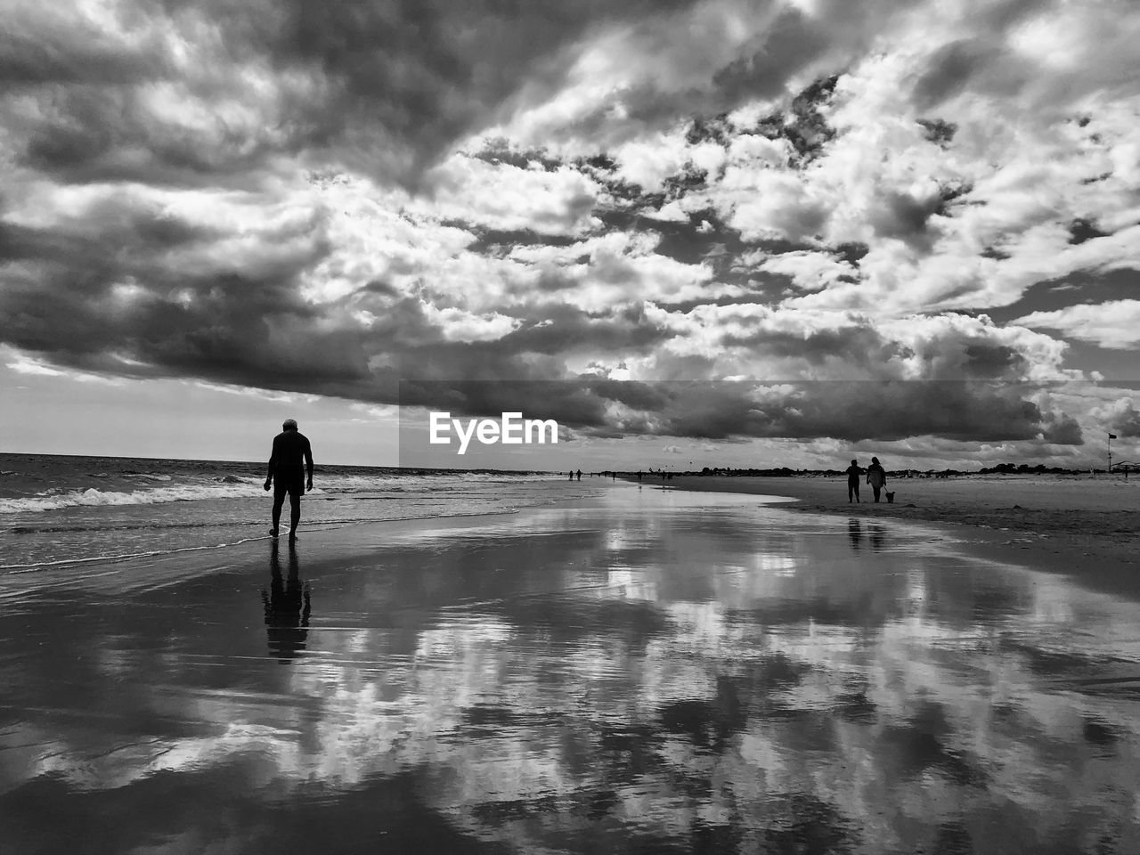 water, sky, cloud, beach, sea, reflection, land, black and white, nature, beauty in nature, horizon, monochrome photography, monochrome, scenics - nature, wave, men, shore, silhouette, leisure activity, ocean, lifestyles, tranquility, holiday, adult, one person, trip, day, vacation, full length, outdoors, tranquil scene, standing, coast, horizon over water, non-urban scene, walking, sand, white, wet