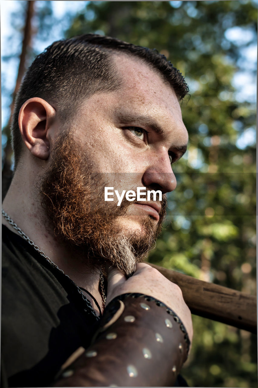 Bearded man looking away against tree