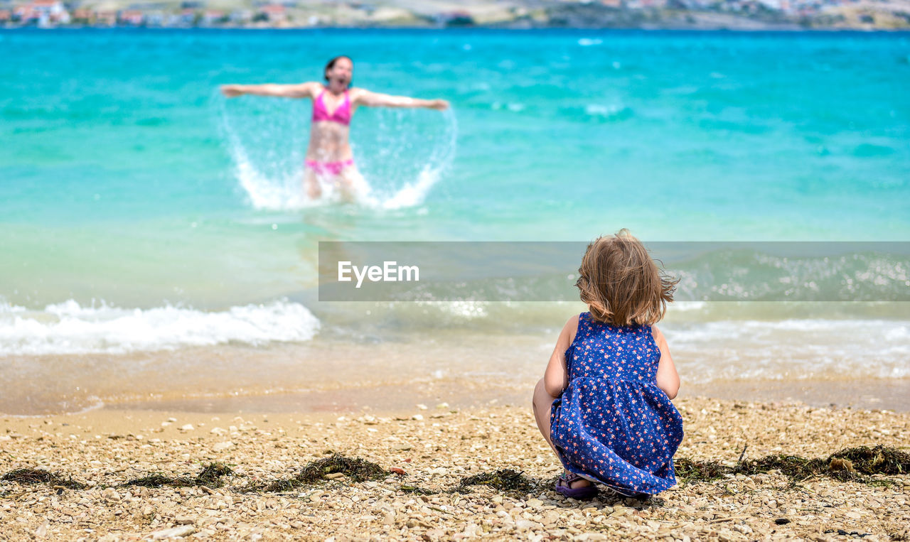 Rear view of daughter looking at mother enjoying in sea