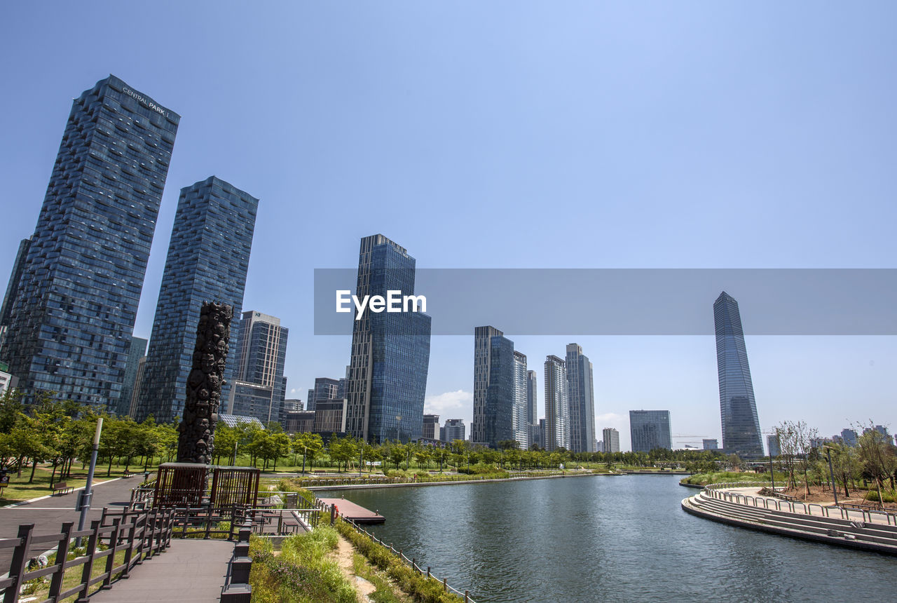 View of lake by modern buildings against blue sky