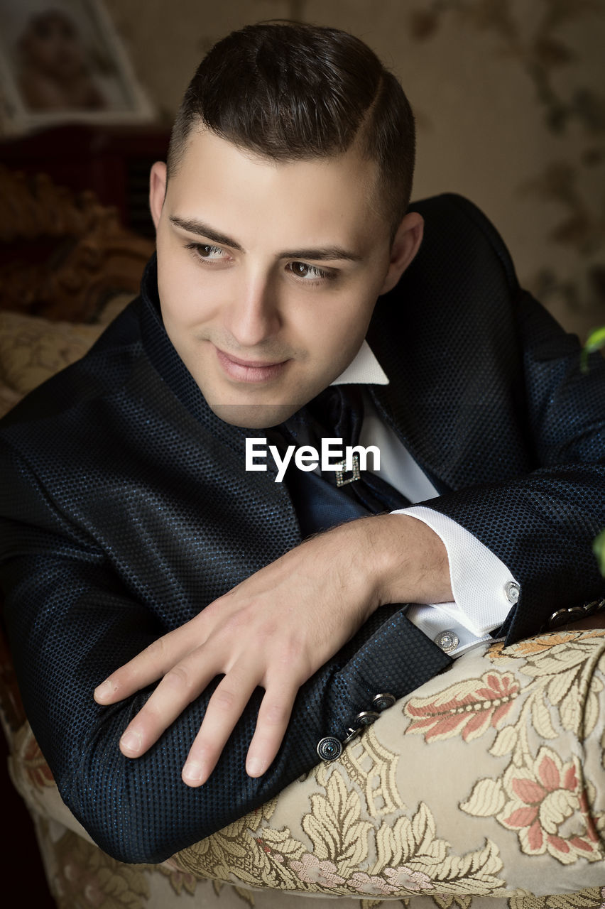 Bridegroom looking away while sitting on sofa