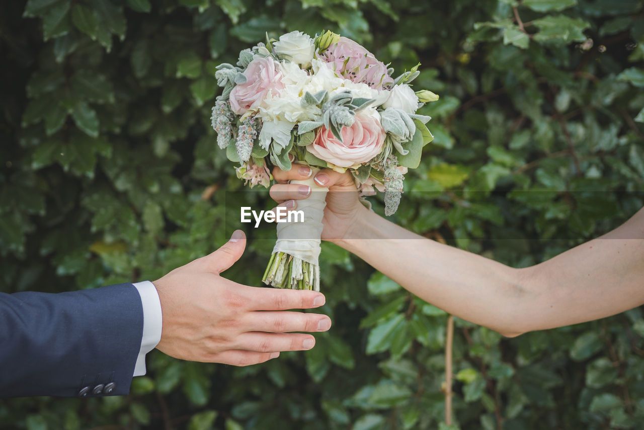 Cropped hand of bride giving bouquet to groom