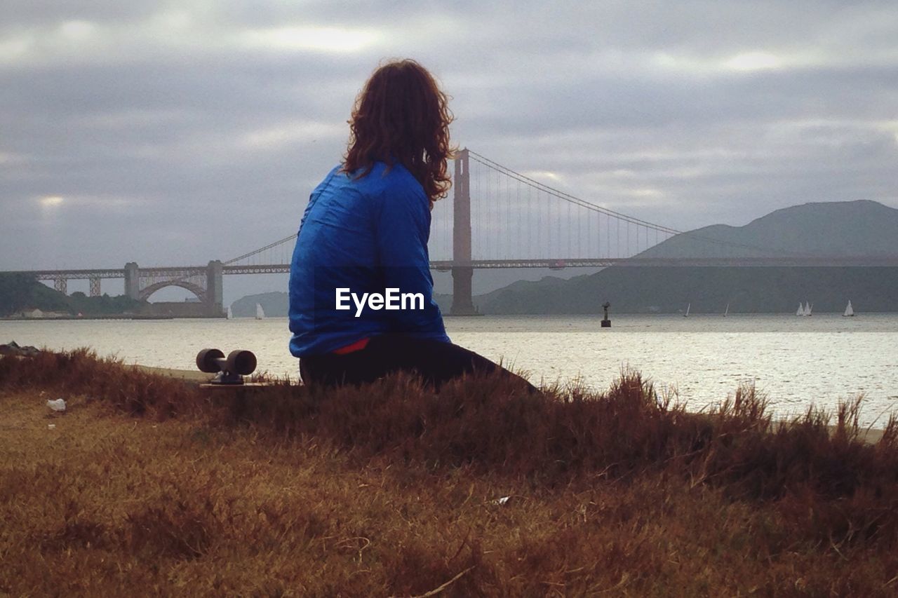 Rear view of woman looking at suspension bridge against sky