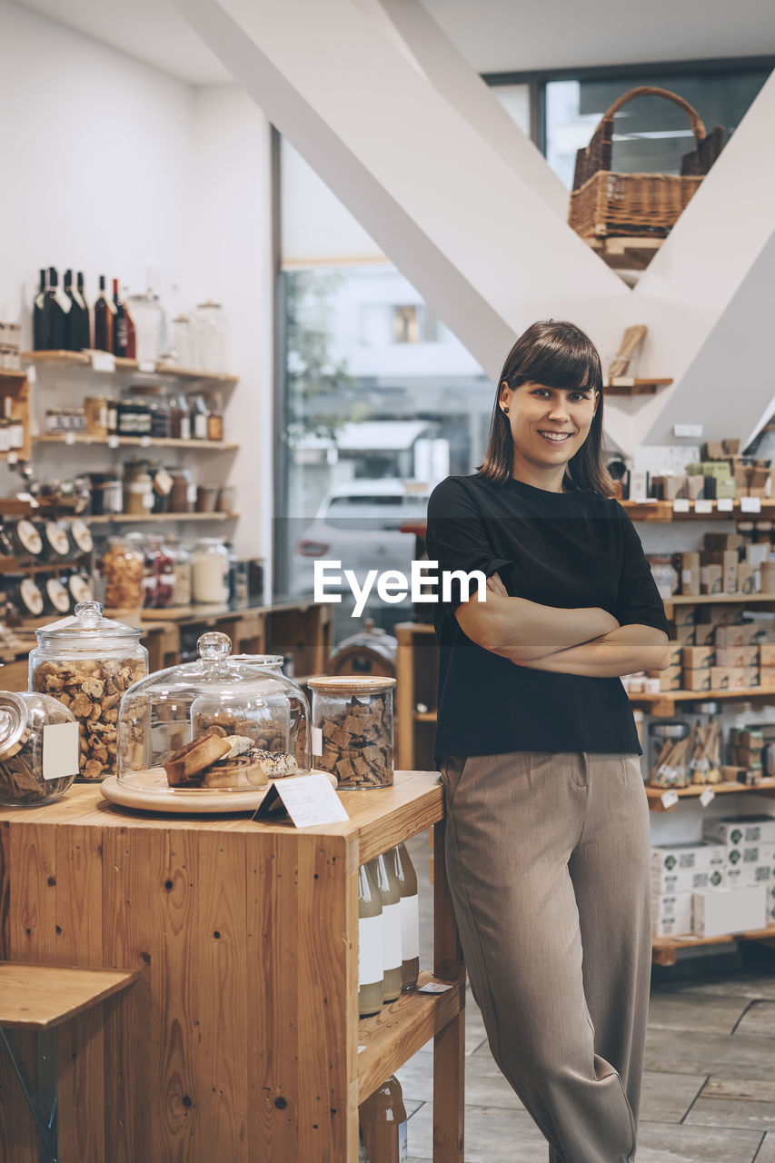 Smiling entrepreneur standing with arms crossed in convenience store