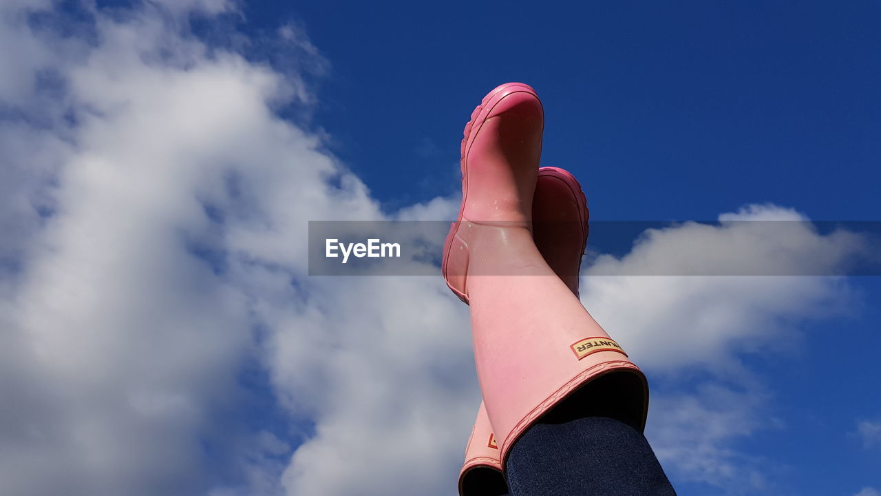 Low section of woman wearing pink rubber boots against sky