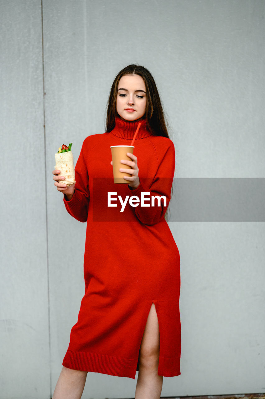 A girl in a red dress holds a shawarma and a glass of coffee in her hands. sausages 