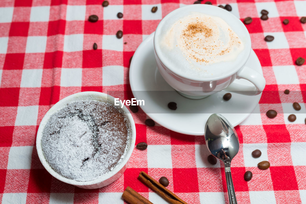 food and drink, drink, coffee, cup, refreshment, mug, kitchen utensil, spoon, coffee cup, eating utensil, checked pattern, tablecloth, crockery, table, saucer, hot drink, food, still life, high angle view, indoors, no people, frothy drink, red, pattern, freshness, cappuccino, studio shot, cafe