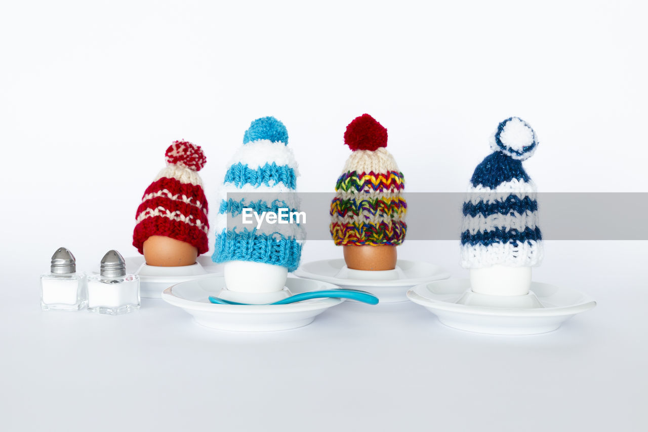 Fun breakfast concept with boiled eggs wearing knitted woolen hats on white background