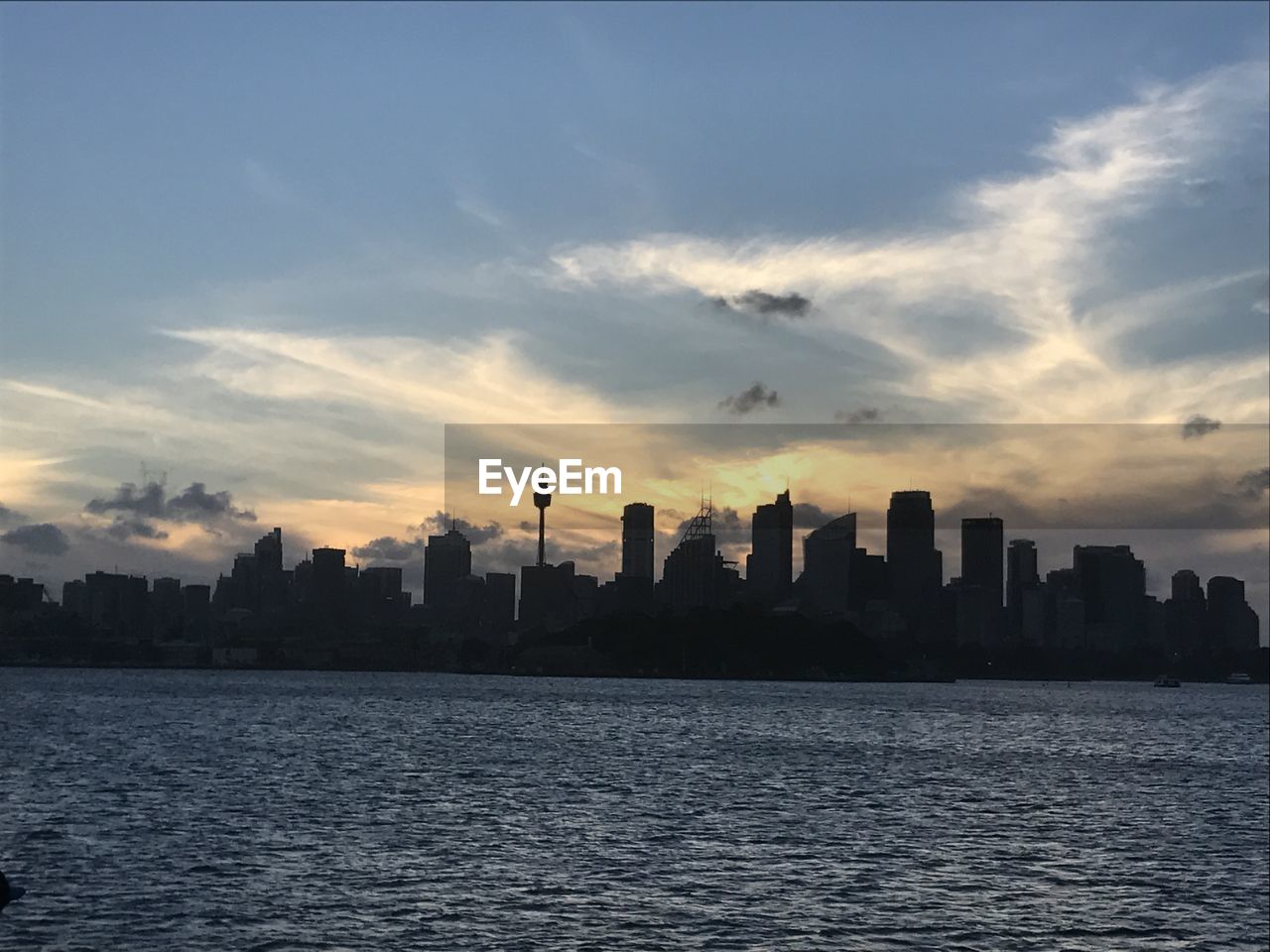 Sea by cityscape against sky during sunset