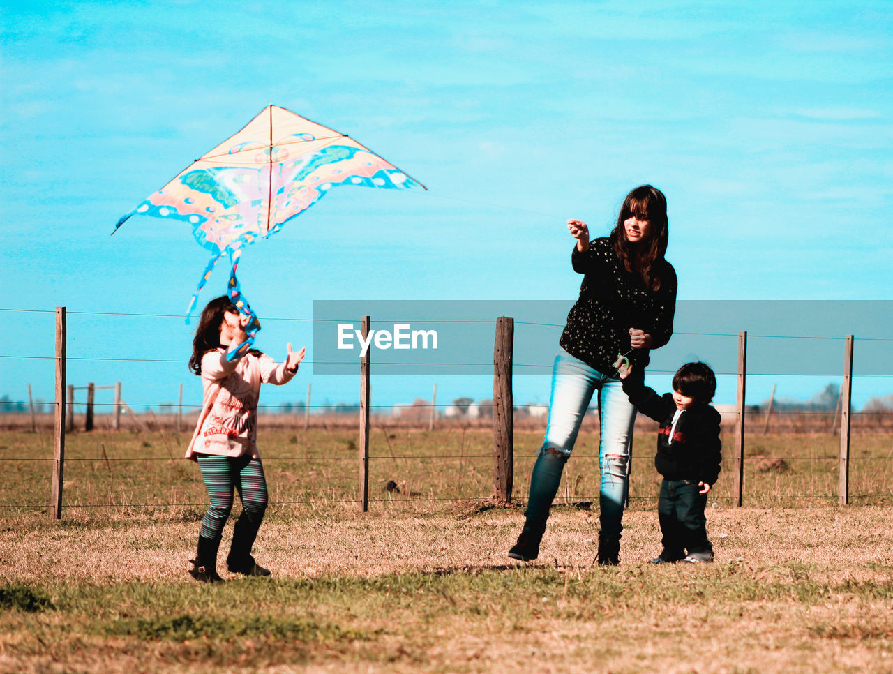 Woman flying kite with children on field against blue sky
