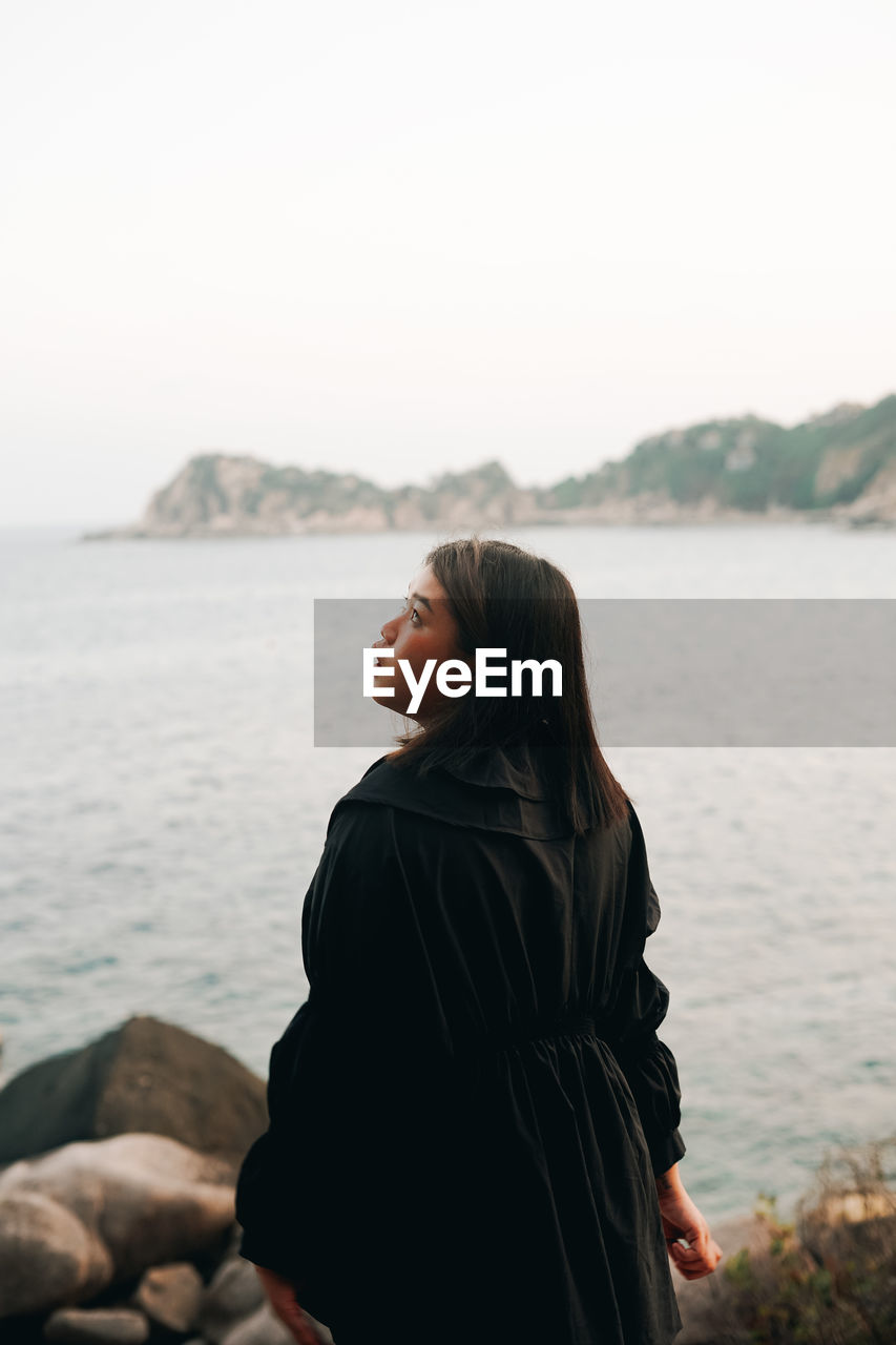 Woman standing by sea against sky