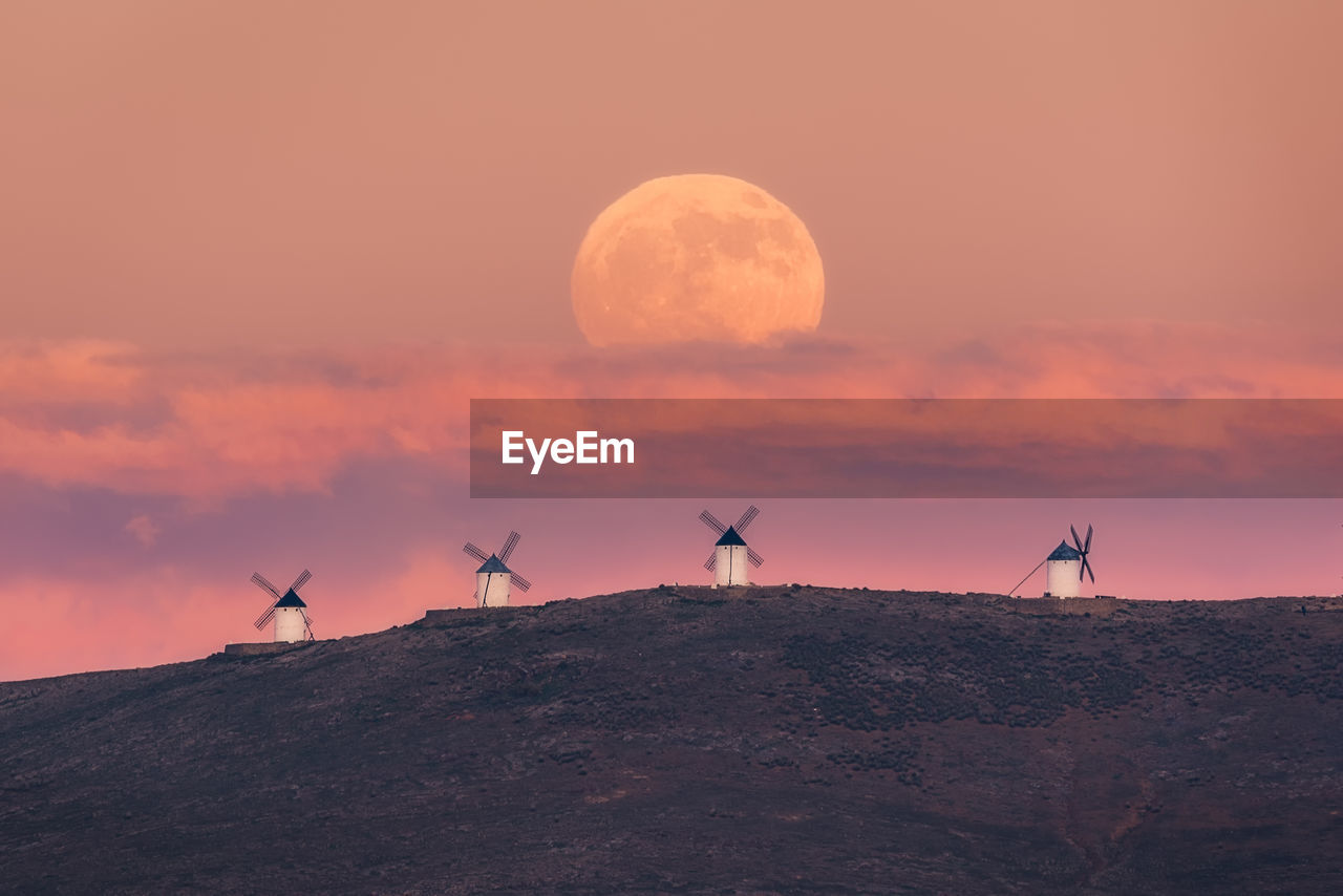 Amazing scenery of majestic full moon over valley with windmills in sundown