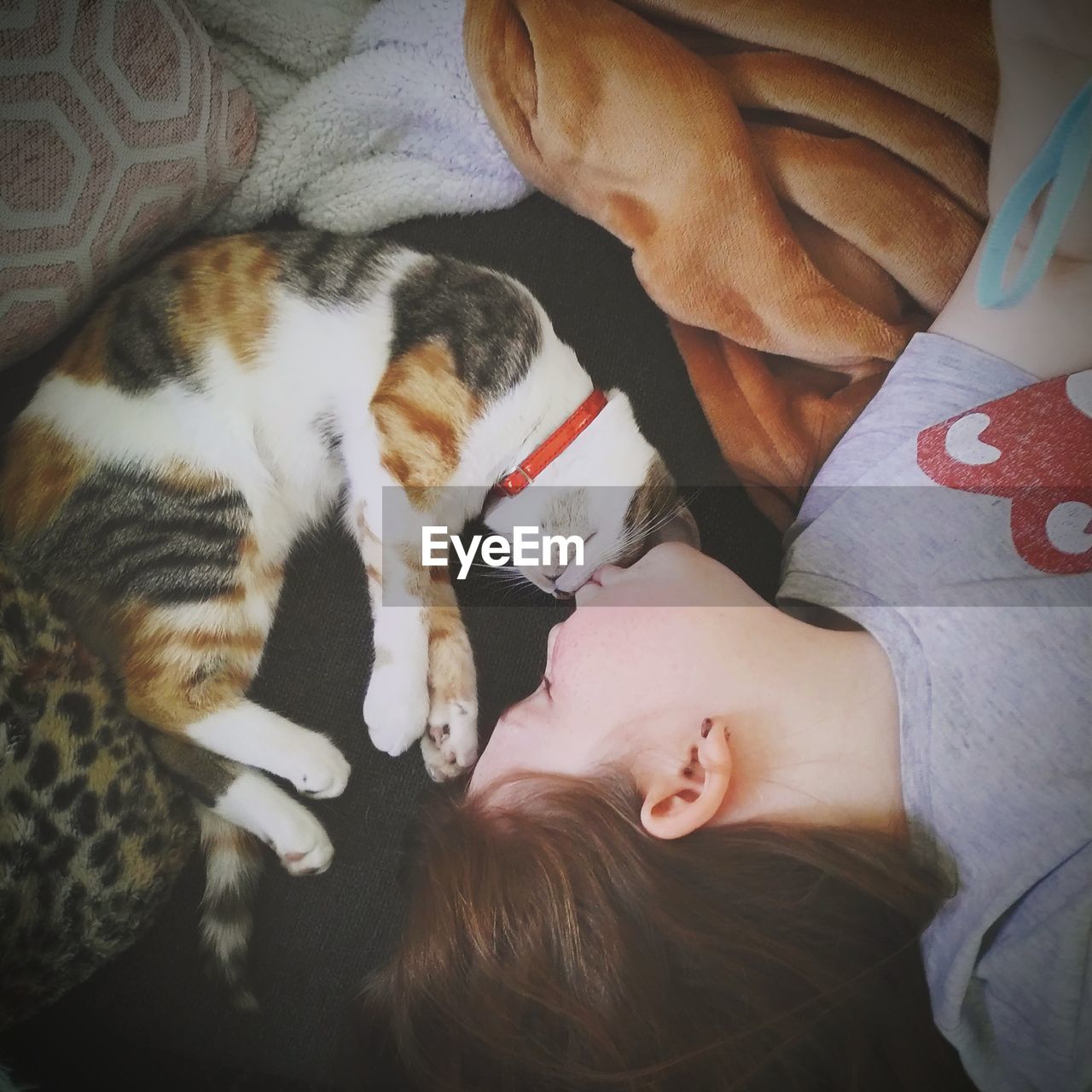 Cute girl kissing cat while sleeping on bed at home