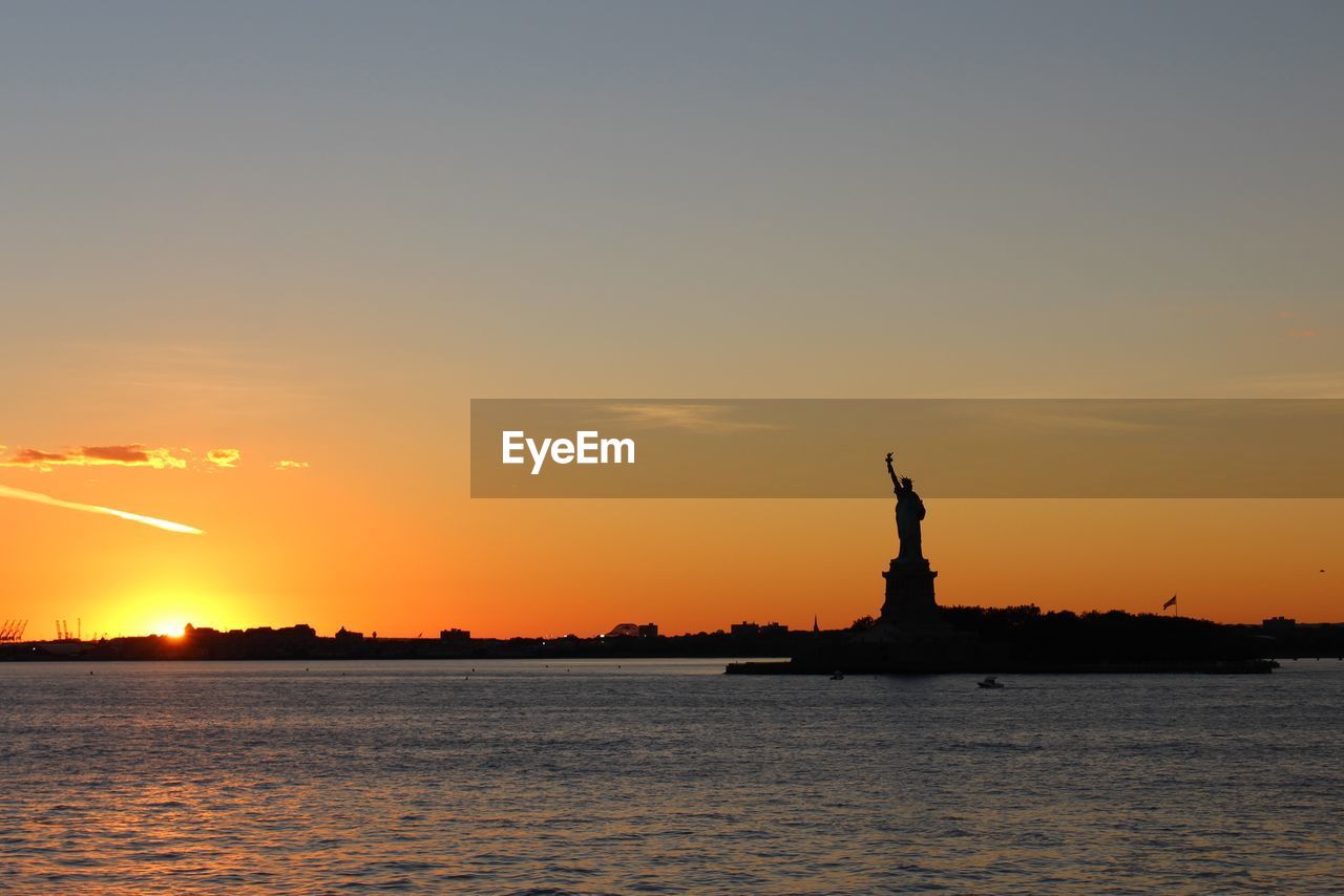Silhouette statue of liberty by sea against sky during sunset 