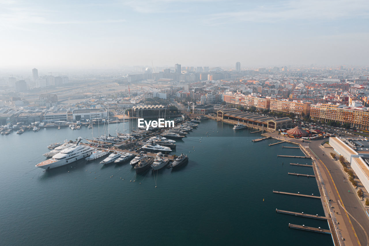 Aerial scenic view of modern city near serene harbor with moored boats in industrial port of valencia