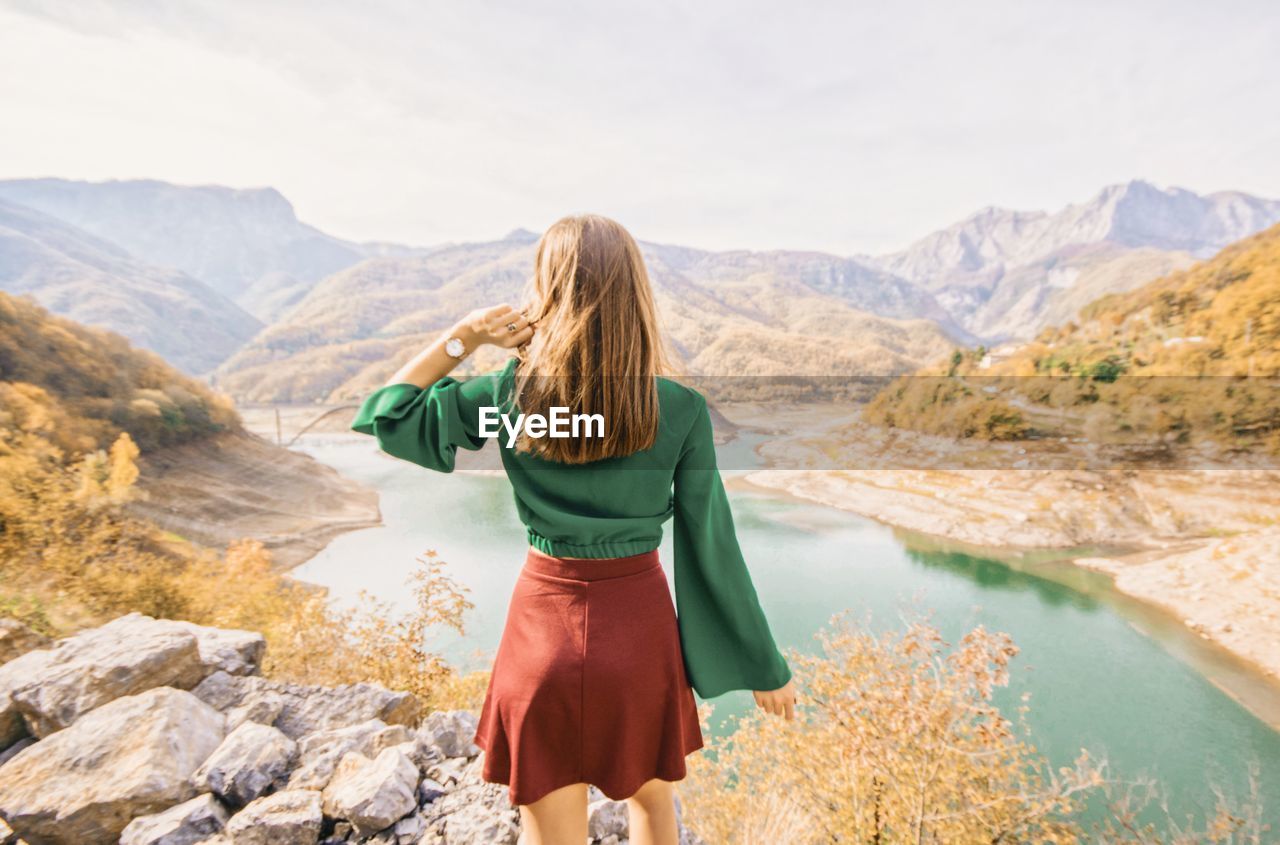 Rear view of woman standing on cliff against sky