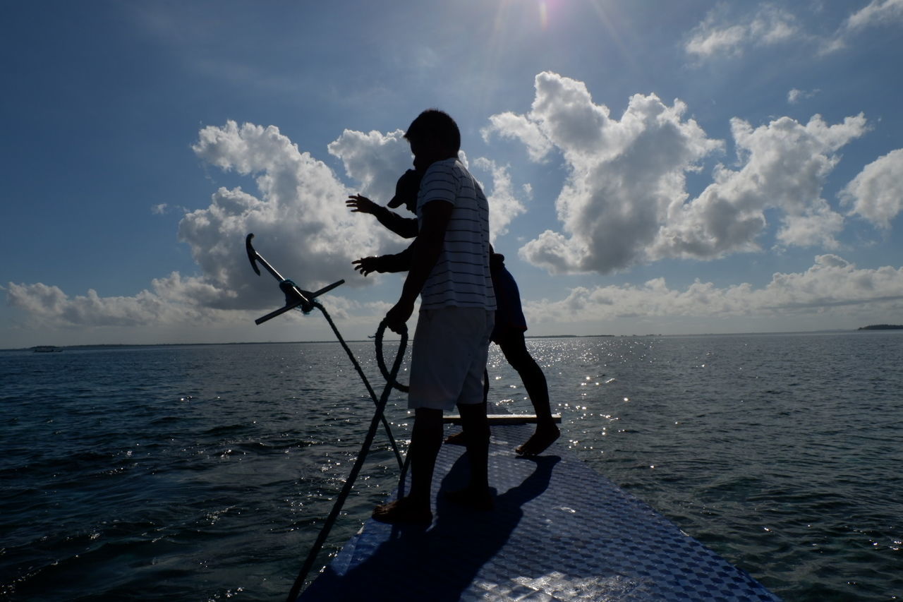 Fishermen standing on boat in sea against sky