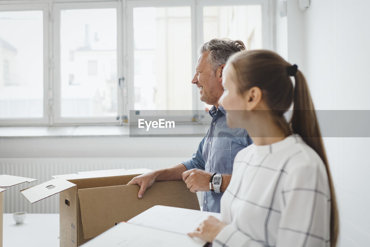 Smiling mature businessman with cardboard box standing by female colleague in new office