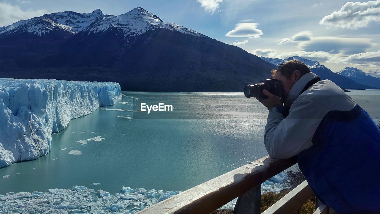 Man photographing iceberg against sky