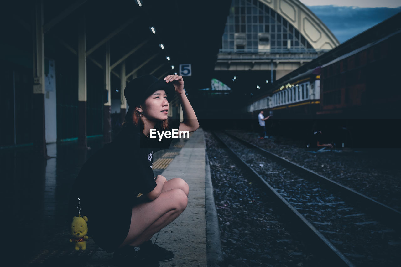 Full length of young woman crouching at railroad station platform