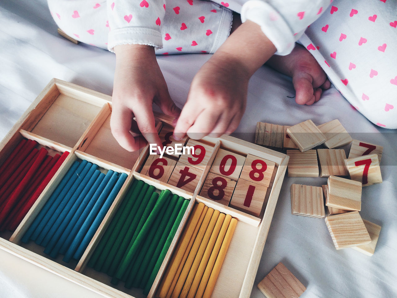 High angle view of child arranging blocks with number in box on bed