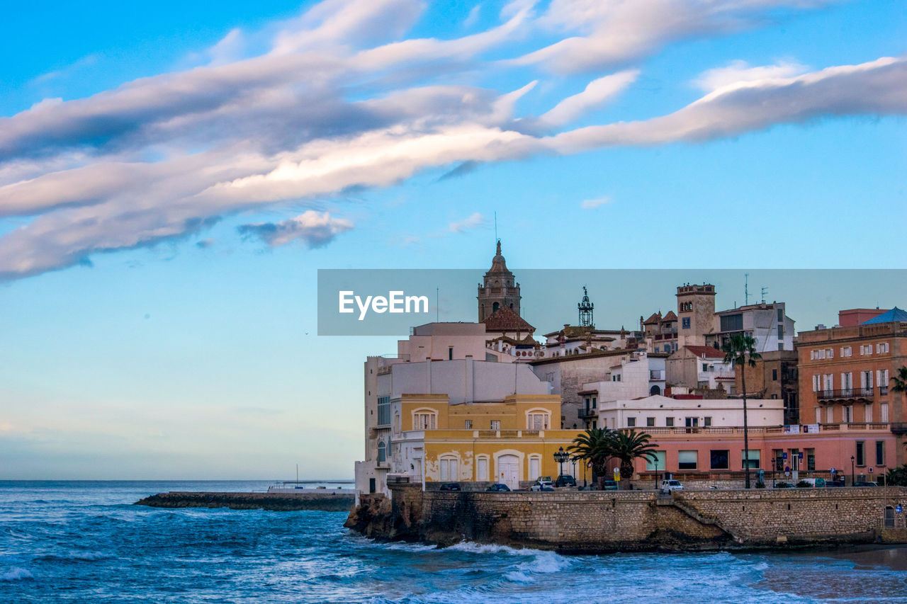 View of building by sea against cloudy sky, in sitges