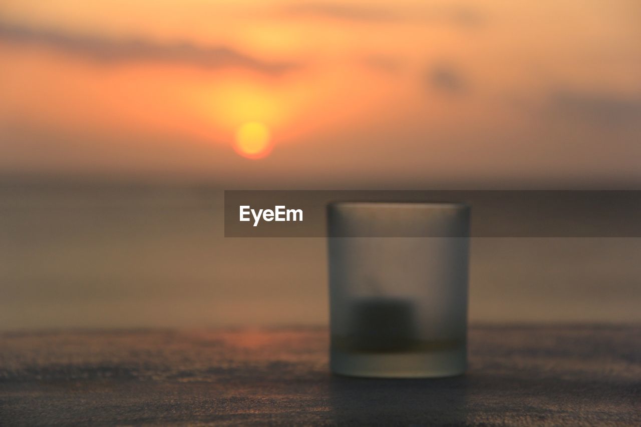 Close-up of glass on shore during sunset