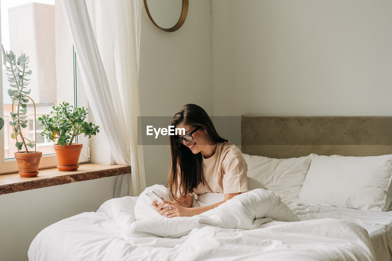 A beautiful brunette young woman checking on her phone after waking up in the morning