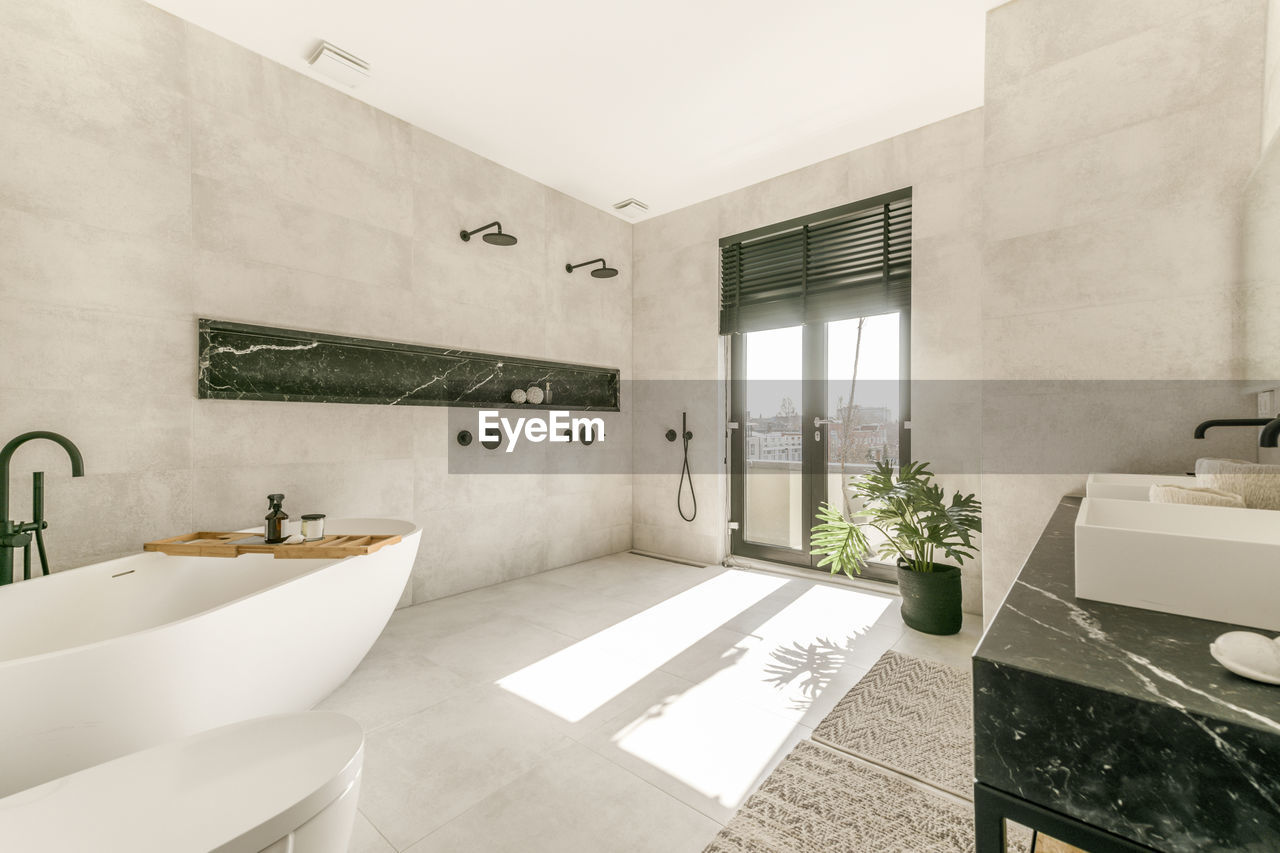 Modern interior of bathroom with white bathtub and ceramic wall mounted toilet and double sinks in minimal style