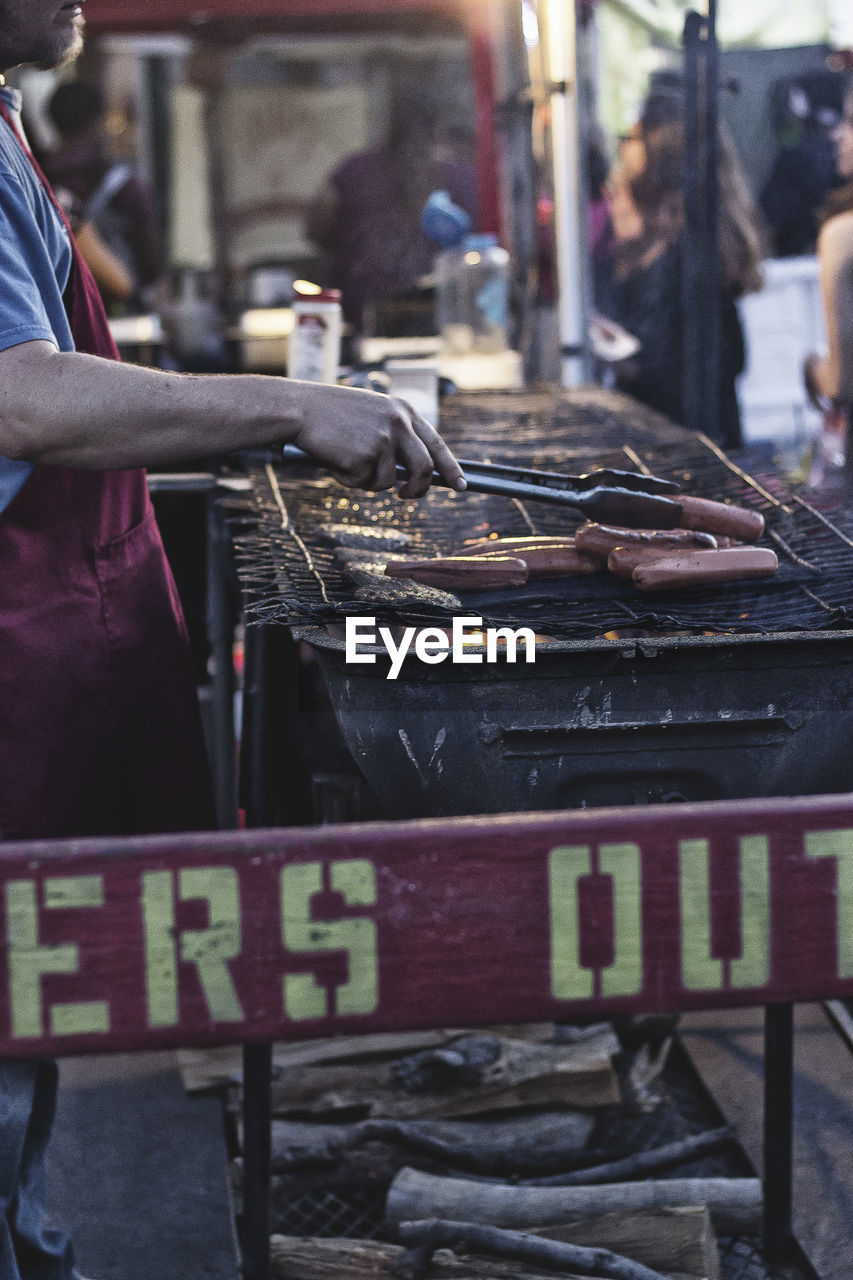 Cropped image of vendor roasting sausages on barbecue