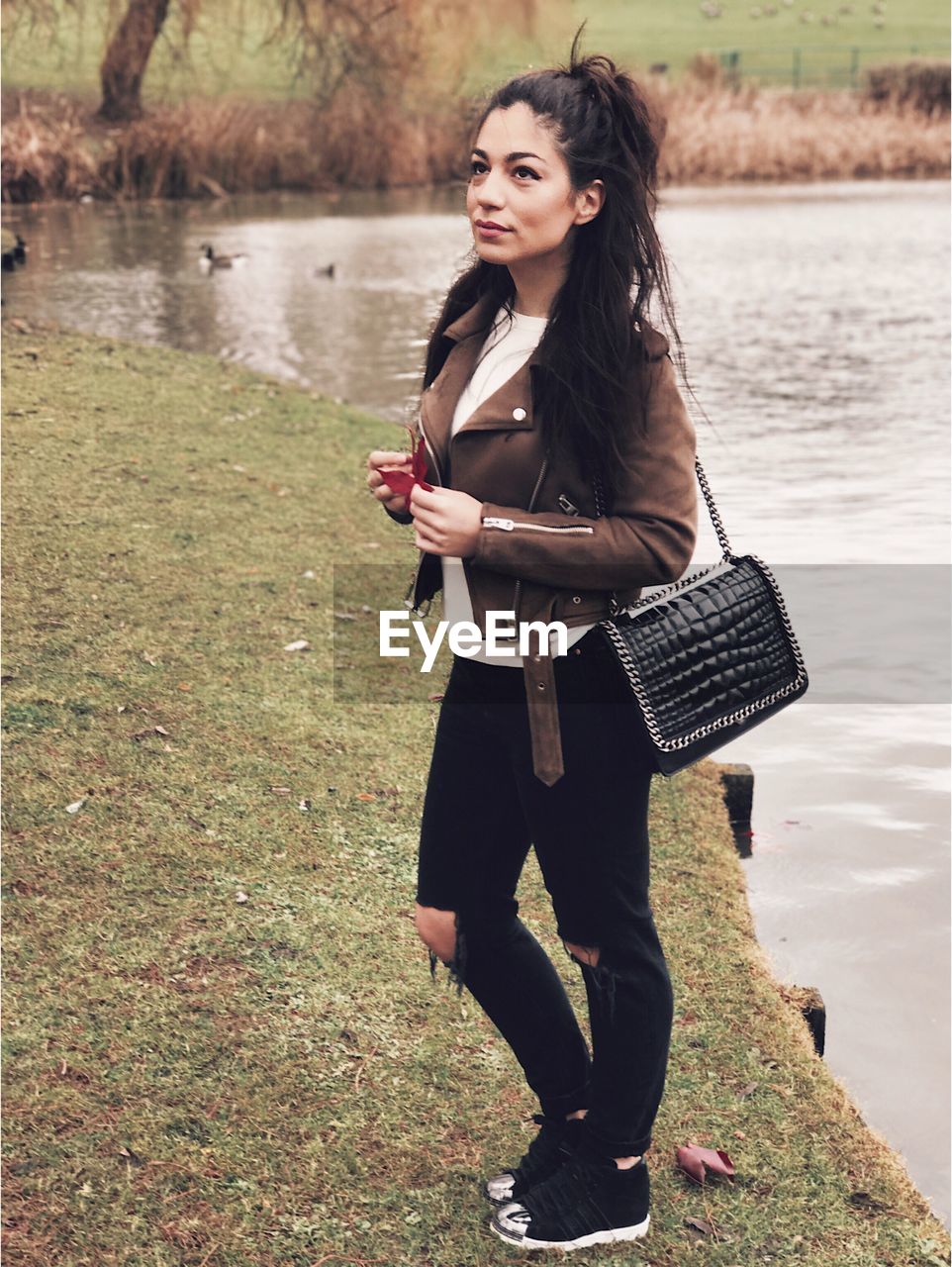 Full length of young woman standing by lake on field