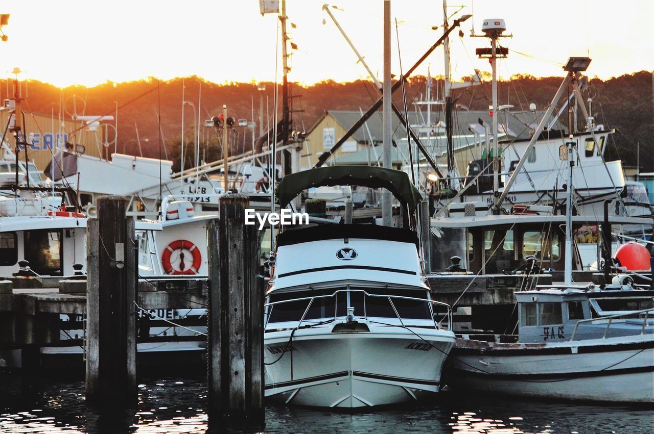 Boats moored at harbor against sky during sunset