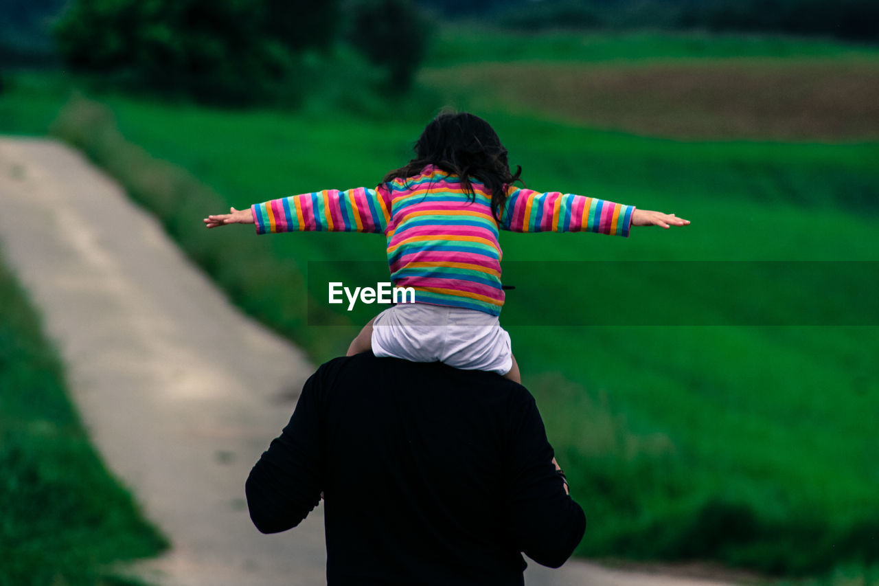 REAR VIEW OF BOY STANDING ON GRASS IN PARK