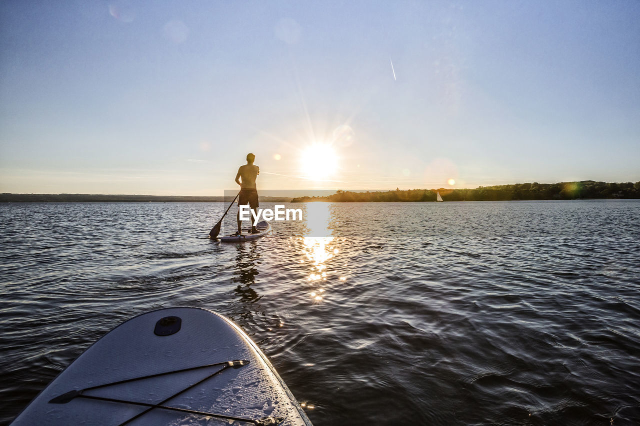 Man paddleboarding in sea against sky during sunset