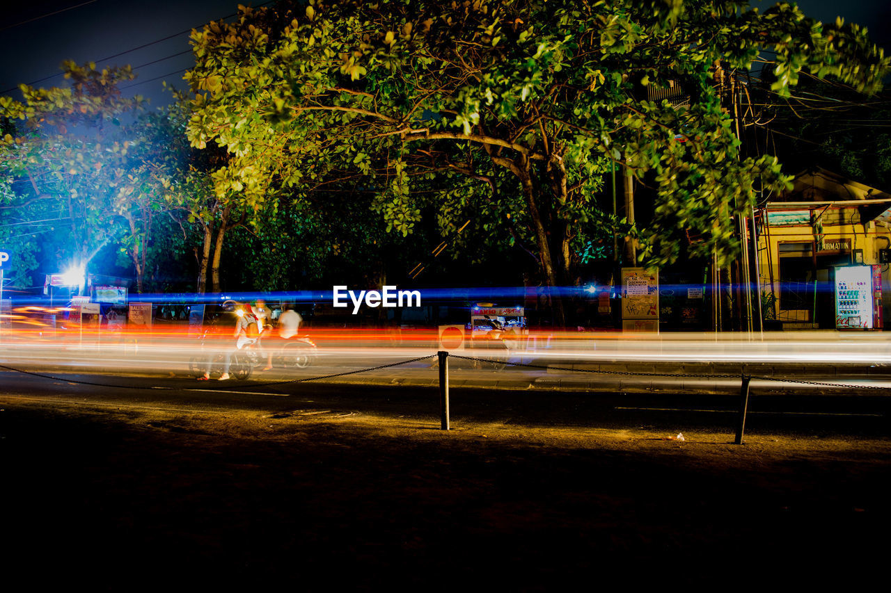 Light trails on road against trees at night