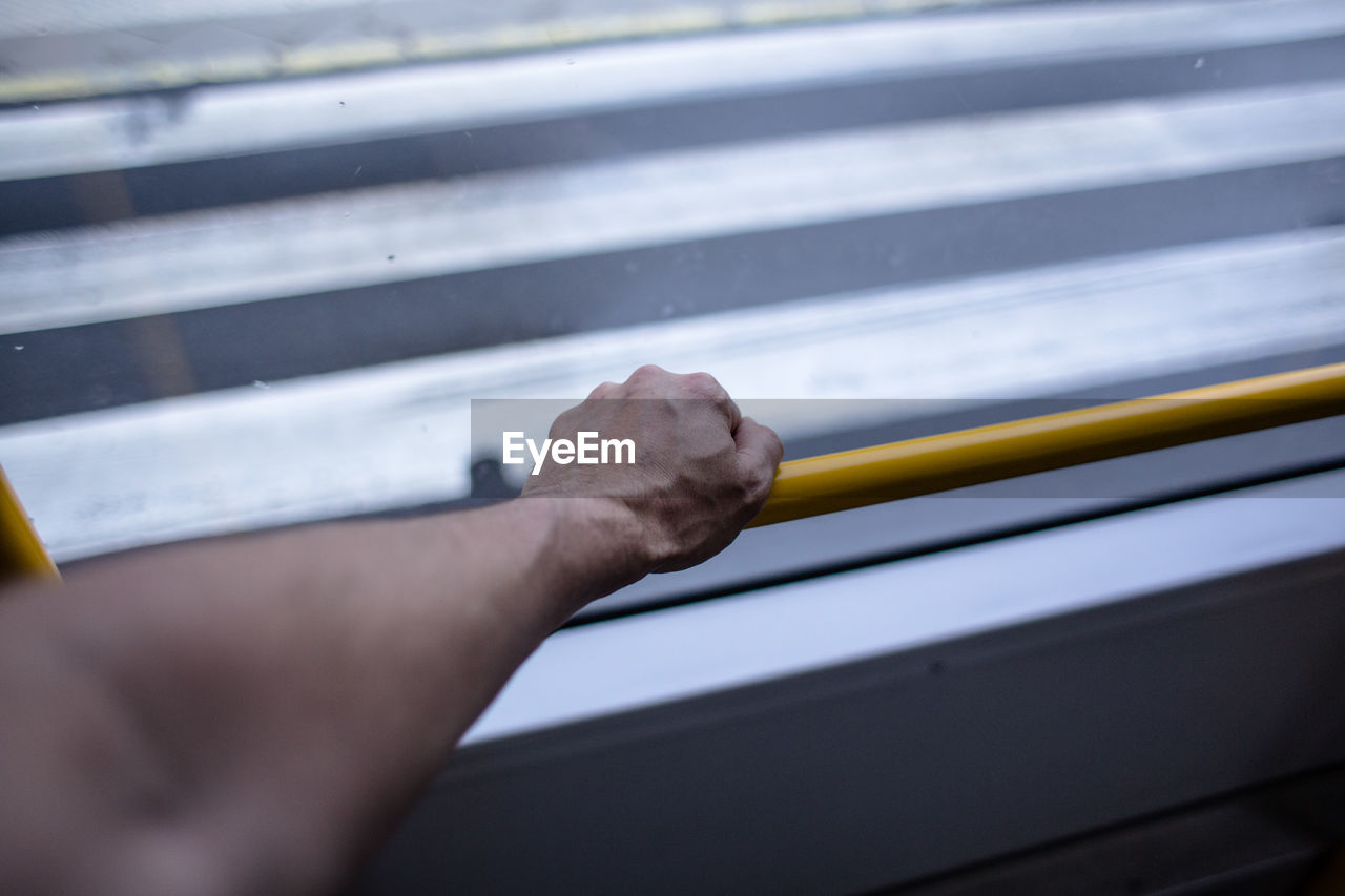 Cropped hand of man holding railing by window