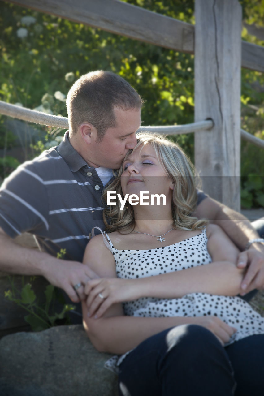 COUPLE KISSING WHILE SITTING ON ROCK