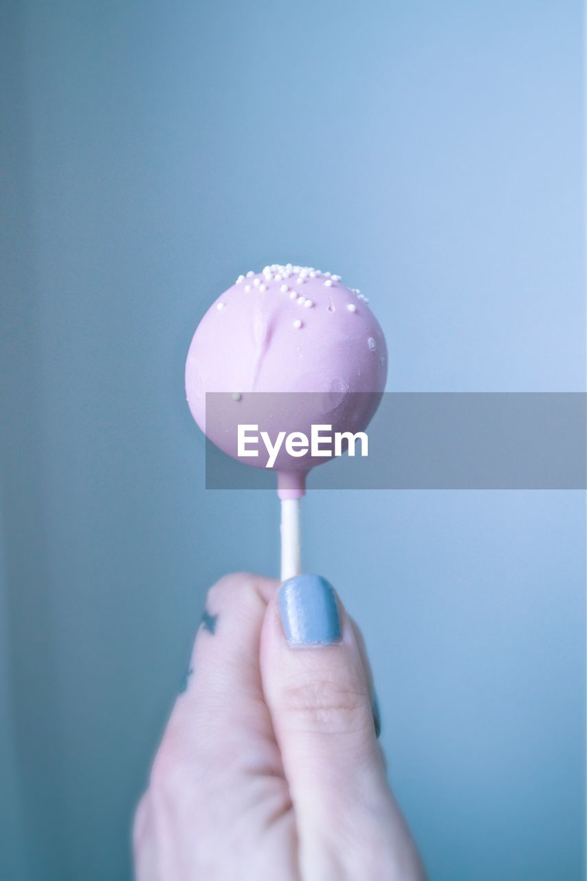 Cropped image of hand holding lollipop against blue background