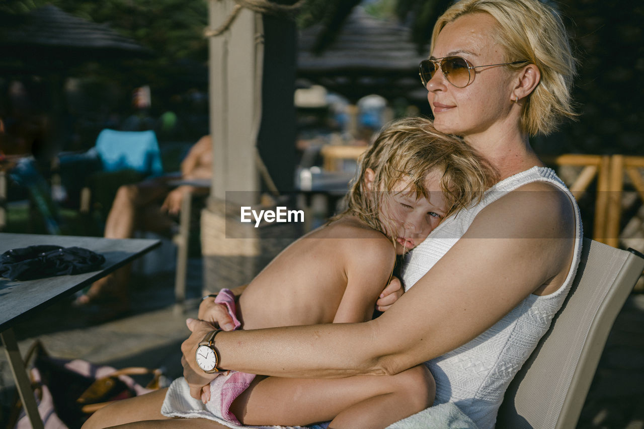 Smiling woman with daughter relaxing on chair at hotel