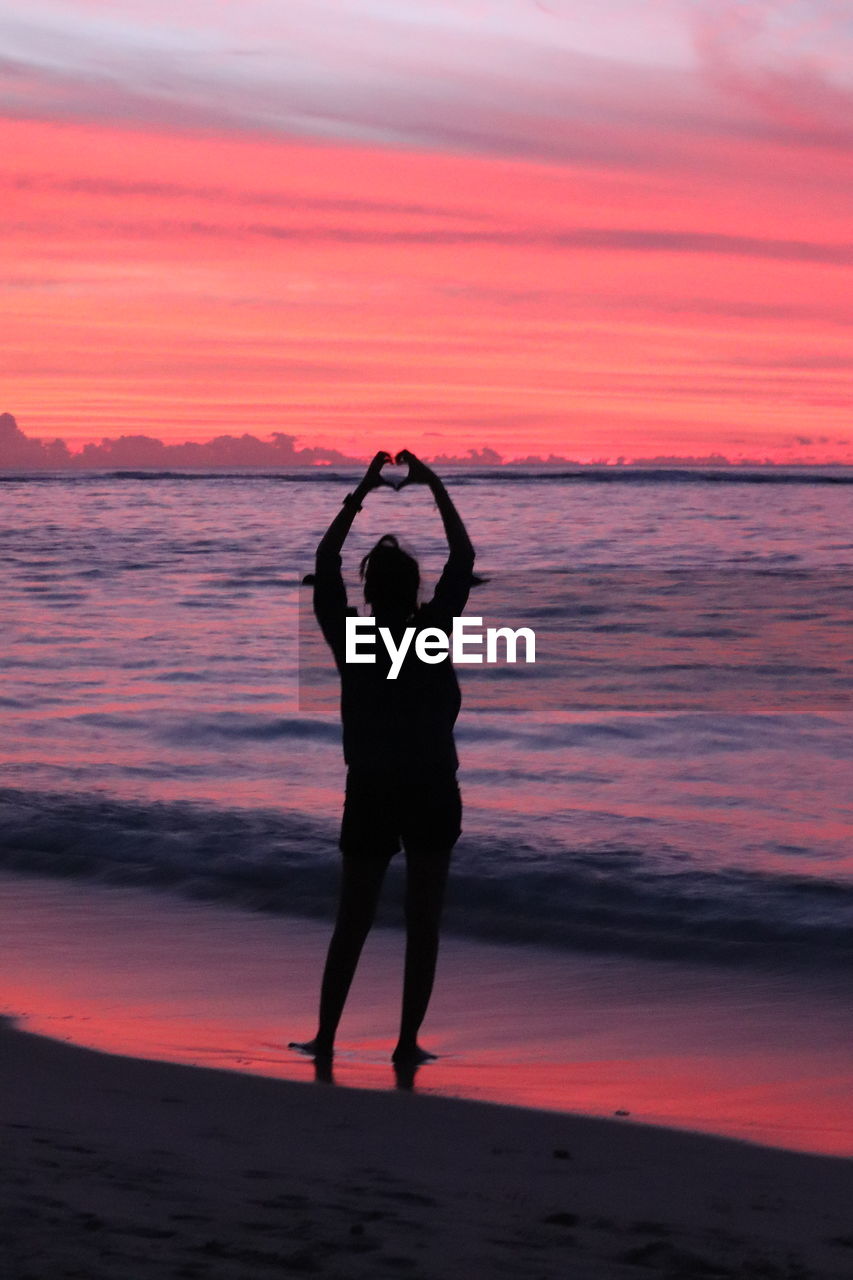 Colourful silhouette photo of a girl standing on the seashore with evening sky