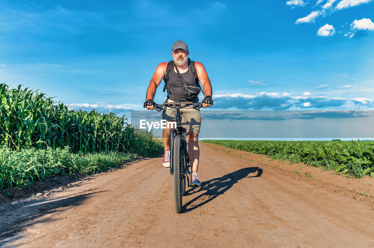 Man with a gray beard rides bicycle on field road. summer bike trip