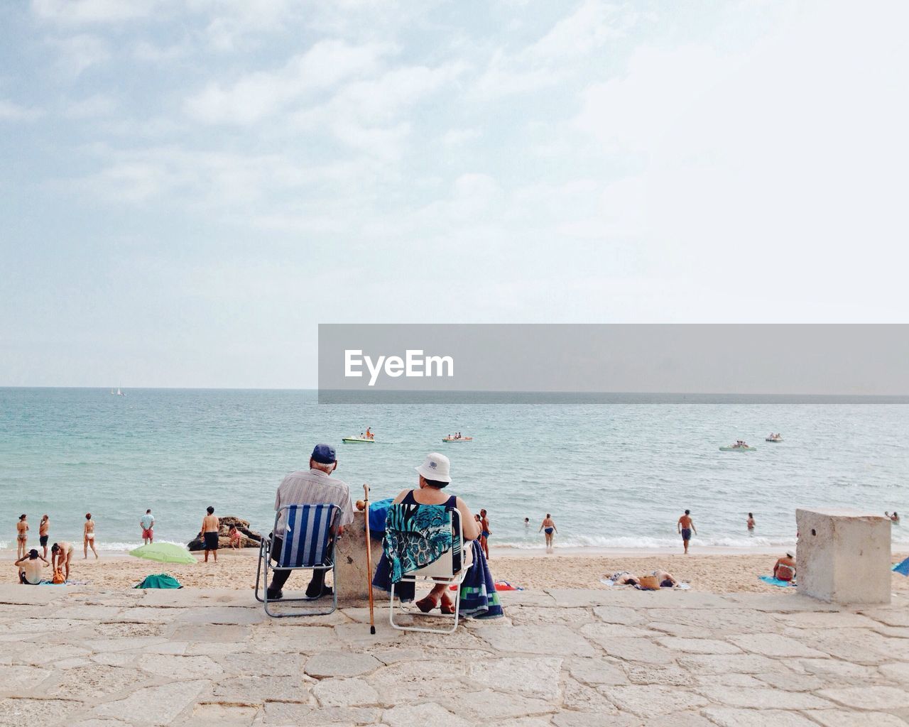 Rear view of man and woman sitting on chair against sea and sky during sunny day