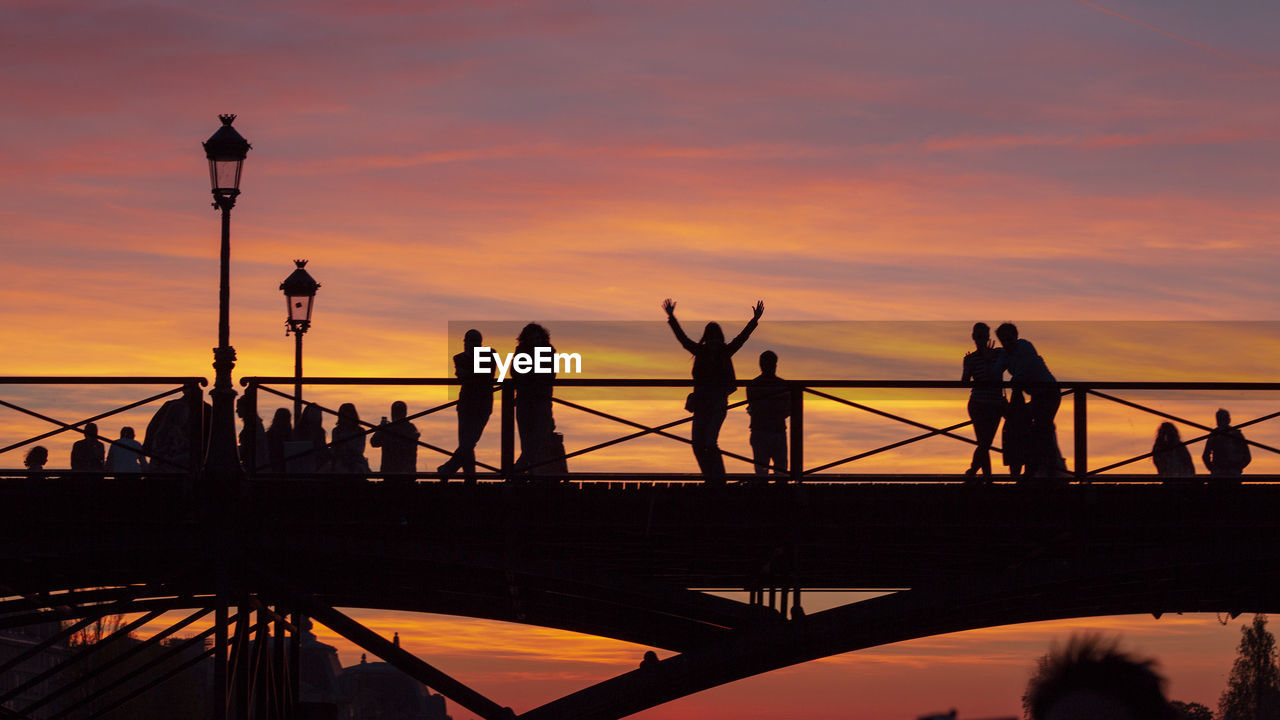 Silhouette people standing on bridge against orange against sky during sunset