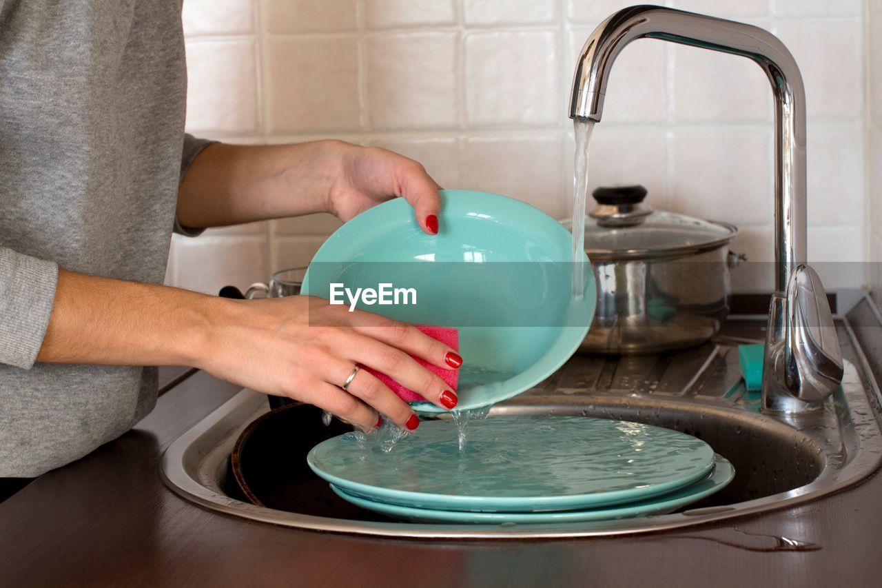 Midsection of woman cleaning plates in kitchen at home