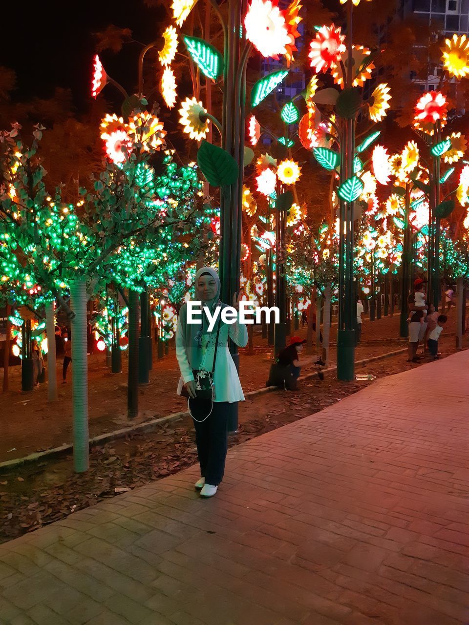 Full length of woman standing at illuminated decorative park on footpath during night