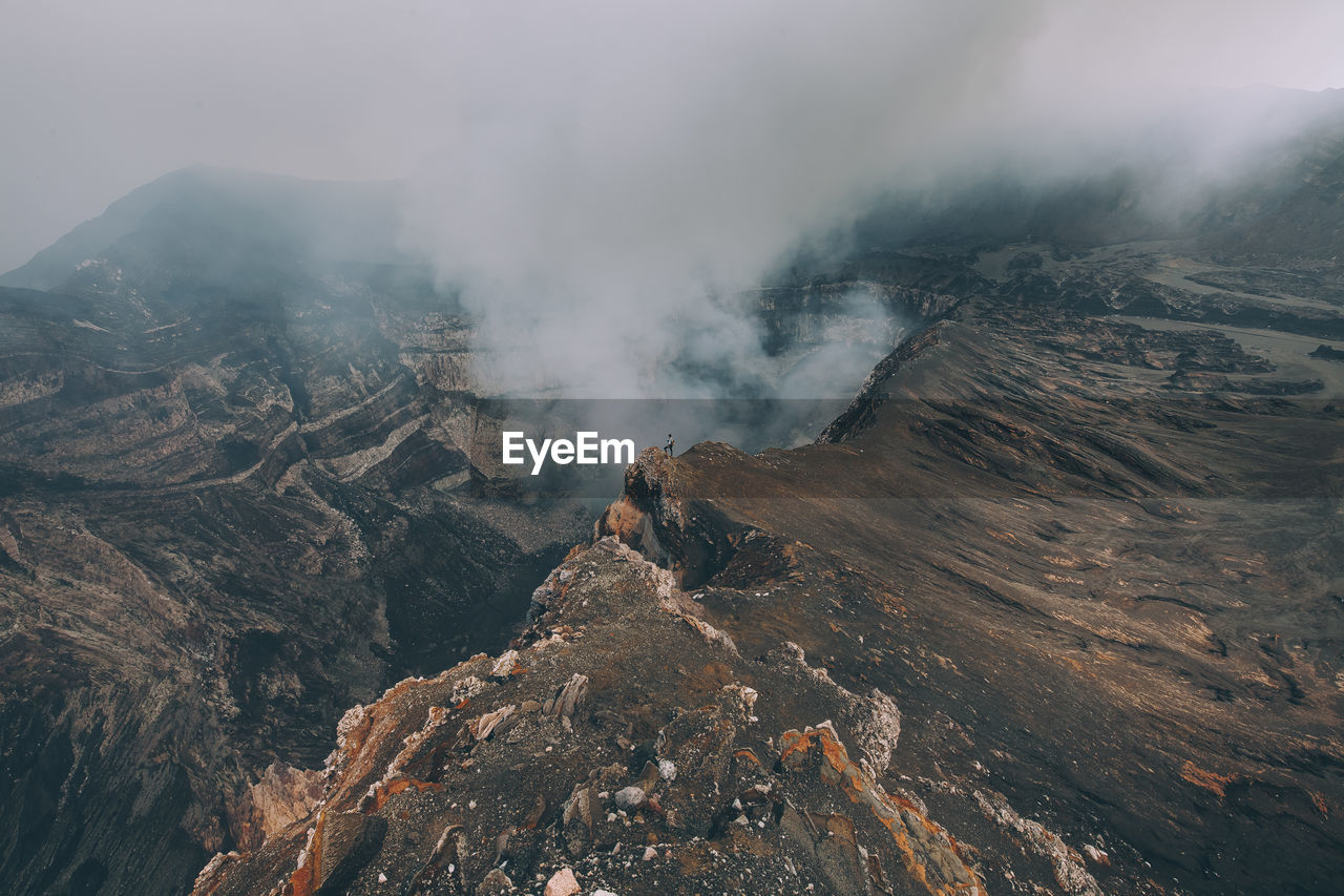 High angle view of woman standing by smoke emitting from volcanic crater